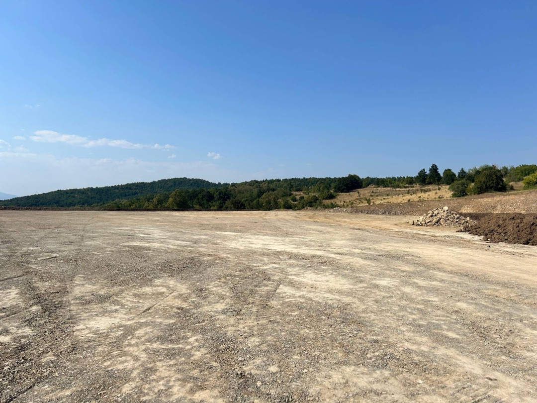 A wide levelled plateau at Malka Golaja, with a heap of stones and an earth bank along the right edge and forest on the horizon; not a single machine in sight.